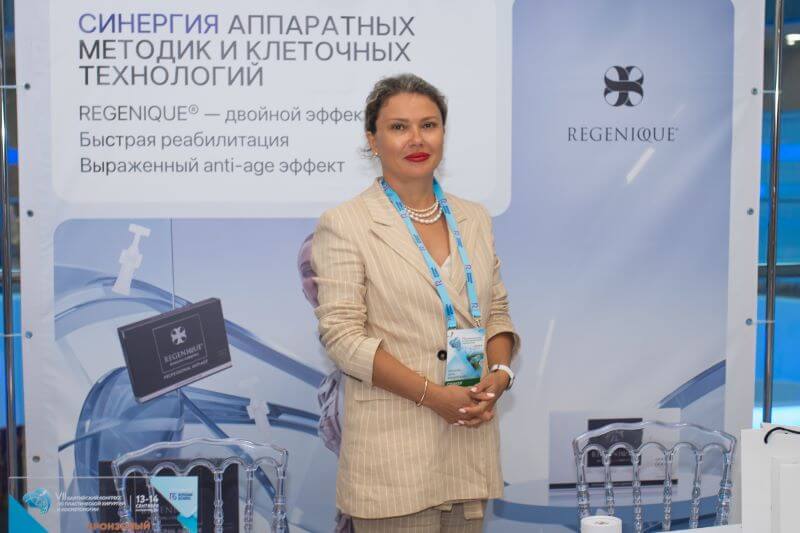 Женщина в деловом костюме стоит перед баннером REGENIQUE.